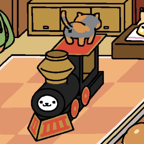 Spooky is a light grey cat with many light orange spots and a tail that is striped with light orange and light grey. Spooky is on top of the cardboard train, facing away from the view, to show its backside. Snowball looks out from where the train's engine should be.