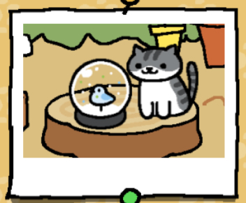 Pickles is a light grey cat with dark grey stripes. The cat's lower face, belly, and paws are white. Pickles looks at the snow dome.