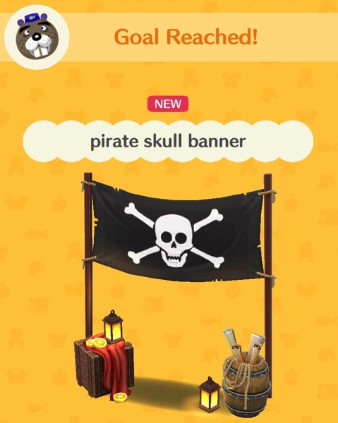 A black banner has a skull and crossbones on it. Each side is held up by tall sticks of wood. Underneath the banner is a box with a red cloth, a lit lantern and a few bells on it. A barrel holds some treasure maps and jewelry. There is a small lantern on the ground next to the barrel.