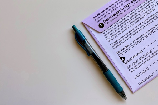 A photo with a mail in ballot that needs to be signed. A pen is next to the ballot. Photo by Tiffany Tertipes on Unsplash