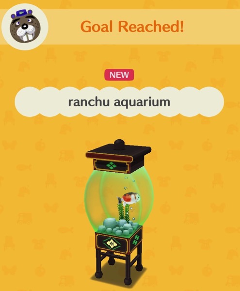 An aquarium with green tinted glass holds a fat ranchu goldfish that is white with orange and black spots. It also holds rocks, a plant, and bubbles.