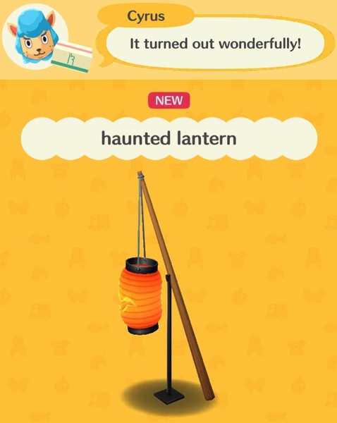An orange lantern that is lit from the inside hangs by a string from the top of a wooden pole. The pole is being held up by a stand. This lantern is haunted.