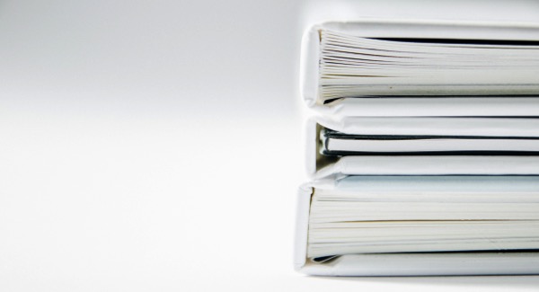 A stack of white binders. Each one appears to be filled with paper. Photo by Beatriz Pérez Moya on Unsplash