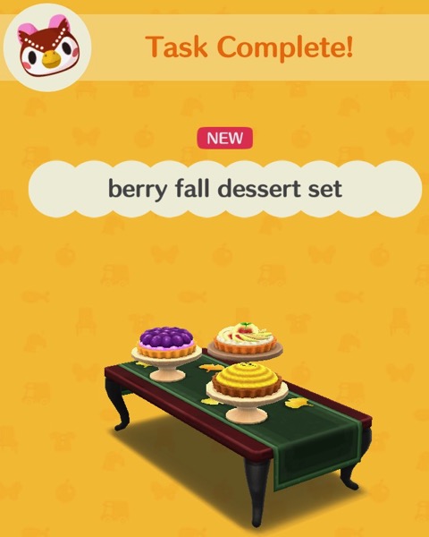 The berry fall dessert set includes a plum pie, an apple pie, and what might be a lemon pie. All are set on raised platters. All of the pies are on a brown wooden table that has a green tablecloth over it.