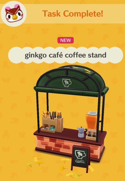 The ginkgo café coffee stand has a red brick base and a metal structure that holds up a canopy over it. The counter has a red top. The counter has a mixer and a small coffee pot. There is a box with paper cups, straws, mixing sticks, and some packets of sugar.