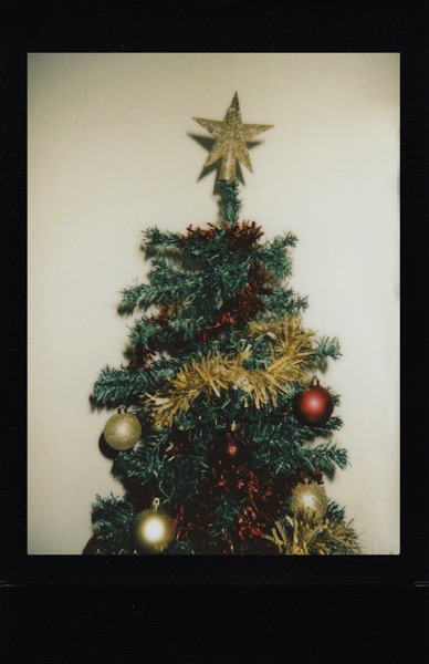 A photo of the top part of what appears to be a plastic Christmas tree. The tree has red and gold garland, red and gold round ornaments, and a glittery star on the top. The photo is bordered by a black frame. Photo by Lisa on Pexels