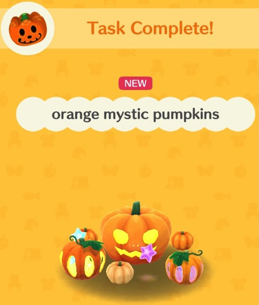 The orange mystic pumpkins are a collection of orange pumpkins of different sizes. The largest one has a carved face with light glowing out of it. Two smaller ones have cutouts that have either yellow or purple light inside. Two tiny pumpkins sit near the rest.