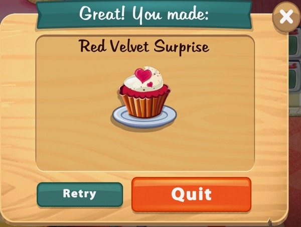 A red velvet cupcake sits on a white plate. The bottom of the cupcake is wrapped in paper. The top of the cupcake is red. It has white frosting with two red hearts on top.