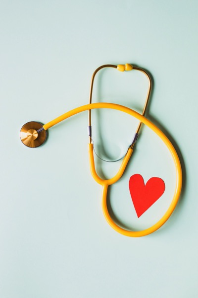 A yellow stethoscope and a red paper heart on a green background. Photo by Karolina Grabowska from Pexels.