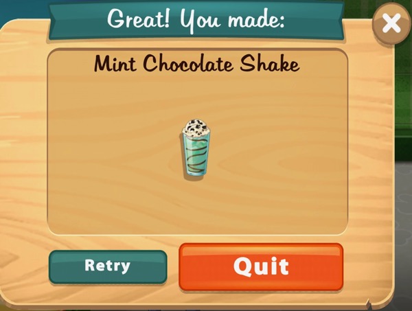 A mint chocolate shake is inside a tall, thin, glass. Most of the shake is green, with a ribbon of chocolate sauce running through it. On top is some whipped cream with broken pieces of chocolate on it.
