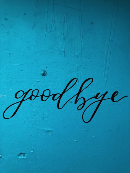The word "goodbye" written in cursive in black paint on a light blue wall. Photo by Renee Fisher on Unsplash.