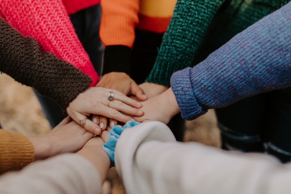 A group of people who are wearing sweaters and putting their hands together. Photo by Hannah Busing on Unsplash