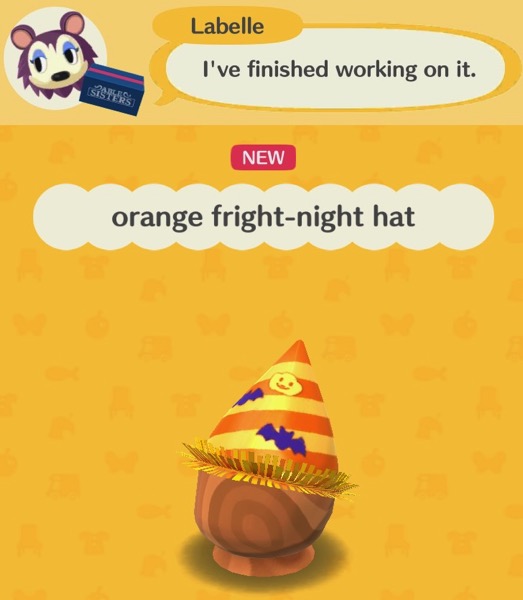 The orange fright-night hat has alternating yellow and orange strips going on a diagonal slant. The top of the hat is cone shaped, and has a yellow pumpkin with a face and two purple flying bats on it. The part nearest the person's face has a yellow decoration that looks itchy.