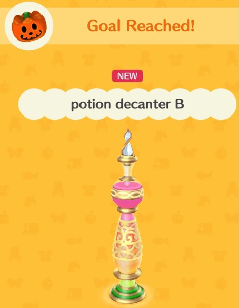 Potion decanter B is shaped just like Potion decanter A. The difference is that Potion decanter B has a bright pink top part which fades to a light orange color toward  the bottom of the bottle. The bottom of the bottle has some gold wire around it, and the inside of that part is green.