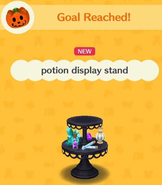 This potion display stand has two, round, tiers. The display is black, and the tiers have black loops decorating their bottom edge. The top tier is empty. The bottom tier has a collection of potions on it - in different shapes, colors and sizes.