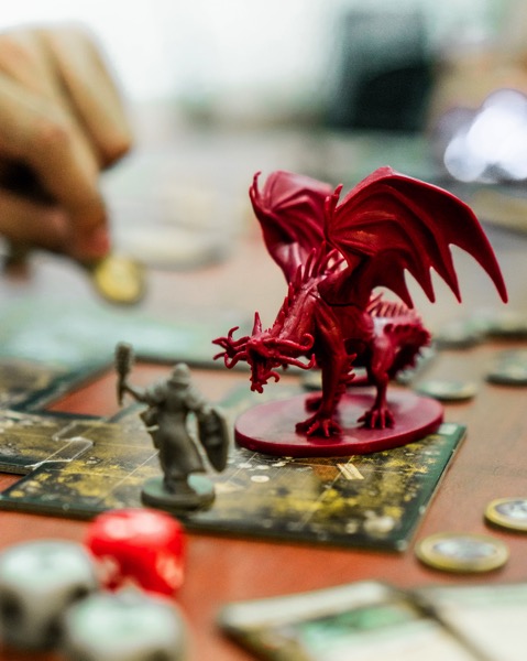 A plastic red dragon looks down at a grey plastic knight. They are standing on colorful tiles that are meant to be a dungeon. Image by Chris Busterillos on Unsplash.