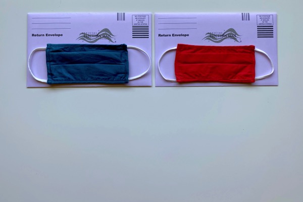 A blue mask and a red mask sit on separate purple envelopes that say Official Election Mail by Tiffany Tertipes on Unsplash