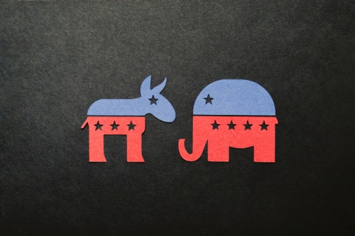paper cut outs of a donkey and an elephant. The top half of each animal is blue, with a star cut-out for an eye. The bottom half of the animals is red, with three star cut-outs on the donkey and four star cut outs on the elephant. Both are on a black background. Image by Kelly Sikkema on Unsplash