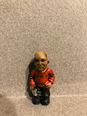 Day Ten gave me Freddy Kruger. His brown face has pock-marks, and his hands are also brown. He is wearing a red sweater with thin, green lines. One of his hands looks like a series of knives. His pants and boots are black.