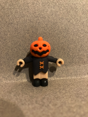 Day Eighteen gave me a scarecrow with a jack-o-lantern for a head. This soft plastic figure is wearing a black shirt with two orange stitches holding the front together. His hands and pants are tan, and his shoes are black. This one has a jack-o-lantern for a head. It is smiling.