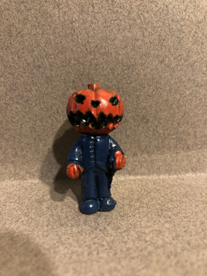 Day Seven gave me a figure that is wearing a carved pumpkin on his head. His clothing is a blueish-grey color. His hands are orange. This is "The Pumpkin King"