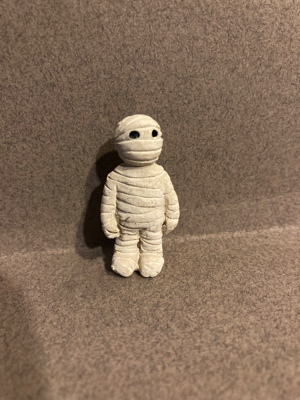 Day Eight is a mummy. This hard plastic figure has a rough texture made by the bandages it is wrapped up in. It has two black eyes. 