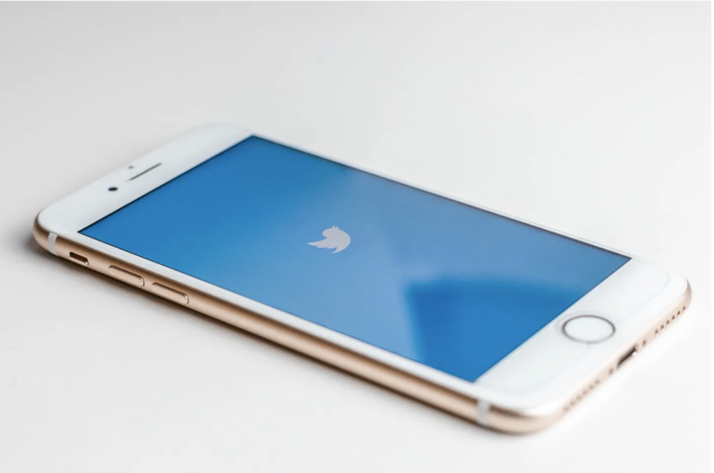 A white smartphone with a blue screen that has the Twitter logo on it - from Unsplash
