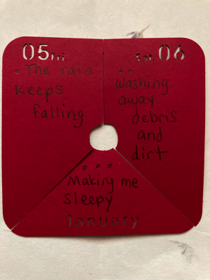 A red piece of paper has a haiku written on it: The rain keeps falling / Washing away debris and dirt / Making me sleepy