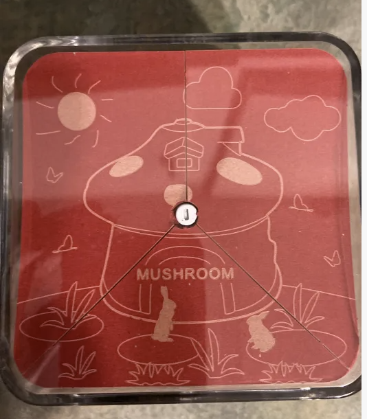 A top-down look at a red piece paper that has three parts. It shows a drawing of a mushroom house. The center of the paper has a metal pipe going through it to hold it all together.