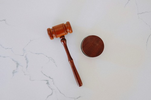 A wooden gavel rests on a marble desk next to a round circle by Tingey Law firm on Unsplash