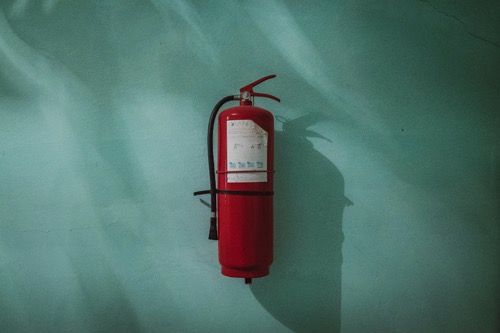 red fire extinguisher on a green wall by Pitor Chrobot on Unsplash
